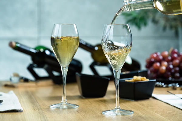 white wine being poured into champagne flutes on a butcher block table with grapes and wine bottles in the background