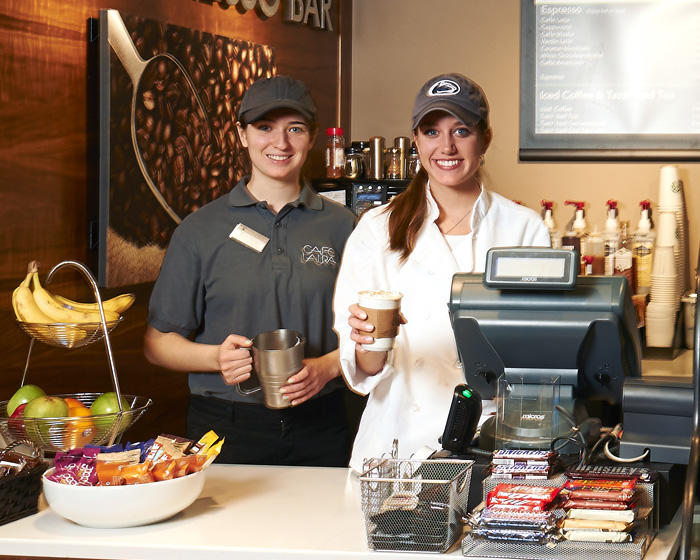 Two employees behind a counter ready to serve a customer a coffee